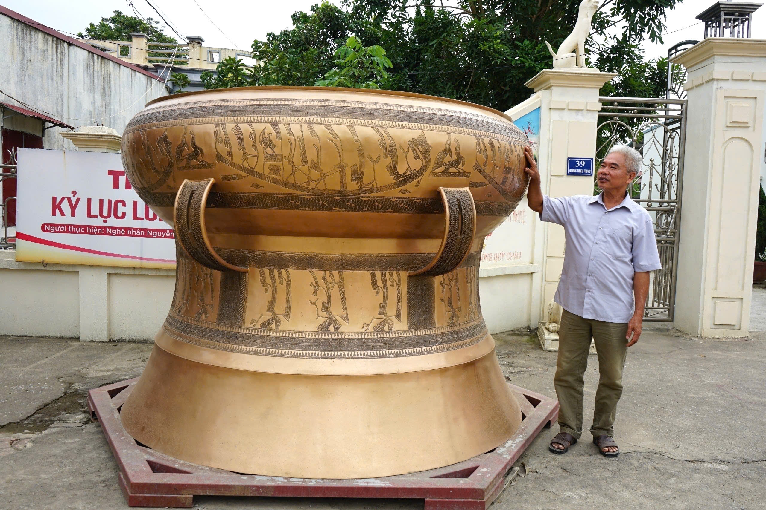 Nghệ nhân Nguyễn Bá Châu bên chiếc trống đồng không lồ do chính tay ông cùng các nghệ nhân lành nghề tạo nên